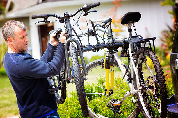 Mature man mounting two  bicylcles on car rack before a family outing. He is lifting a bike and tying it with rubber bands.