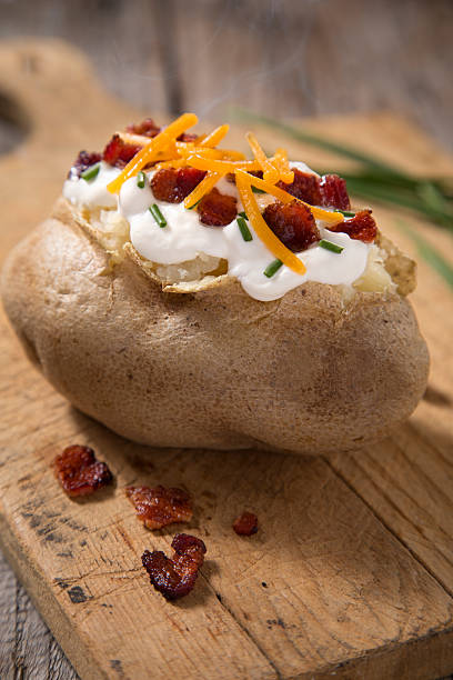 Baked Potato A baked potato with sour cream, bacon, cheese, and chives on rustic cutting block.  Please see my portfolio for other food and drink images. baked potato sour cream stock pictures, royalty-free photos & images