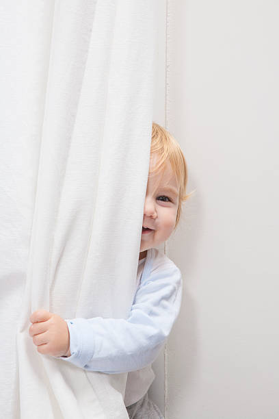 baby peeking behind curtain stock photo