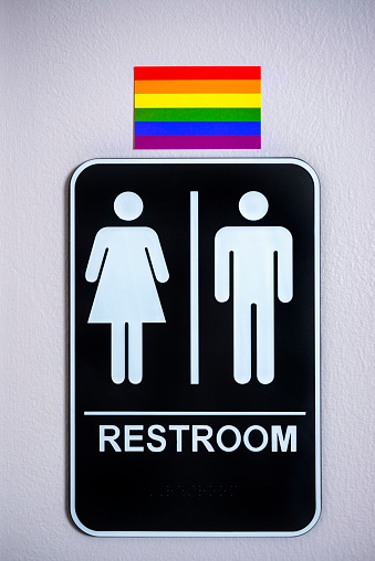 LGBT flag above a restroom sign posted on a wall. There is a lot of controversy over North Carolina's HB2 bill, the Carolina bathroom bill,  and other legislation around the US against the LGBT community.
