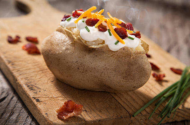 Baked Potato A baked potato with sour cream, bacon, cheese, and chives on rustic cutting board.  Please see my portfolio for other food and drink images. baked potato sour cream stock pictures, royalty-free photos & images