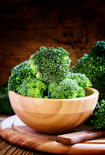 Fresh green broccoli in a wooden bowl on dark wooden background, selective focus