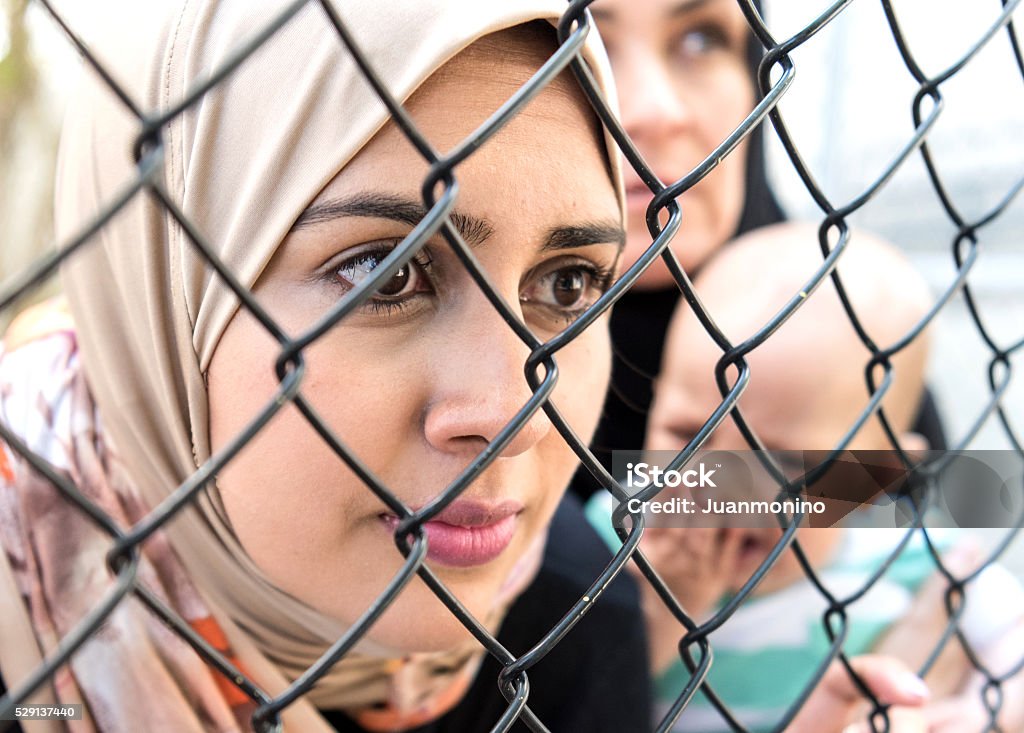Sad refugee Middle eastern women (Real People) Middle eastern women posing looking looking through a fence very sad one is holding a crying baby Refugee Stock Photo