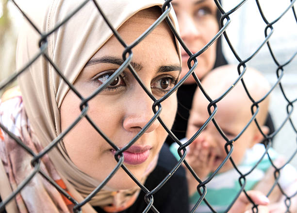 Sad refugee Middle eastern women (Real People) Middle eastern women posing looking looking through a fence very sad one is holding a crying baby iraq photos stock pictures, royalty-free photos & images