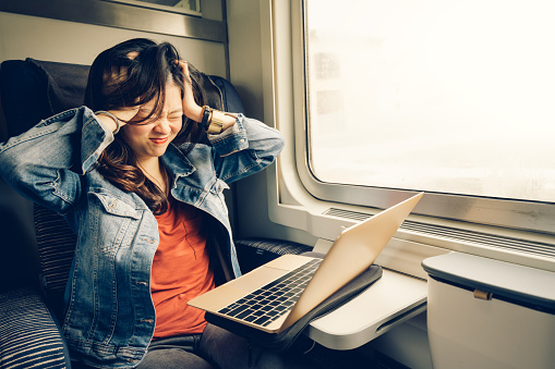 Asian college girl frustrated with laptop on the train, warm light tone, with copy space