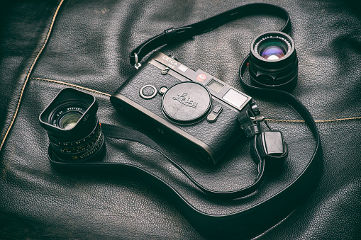 Bucharest, Romania - May 6, 2016: Image of a black Leica M6 camera body with a Summicron 35 mm and a Summarit 50 mm lenses sitting on a black leather surface. Bucharest, Romania, May 6, 2016.