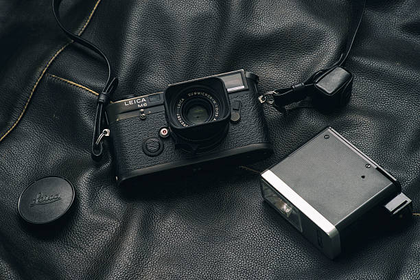 Analog Leica and flash Bucharest, Romania - May 6, 2016: Image of a black Leica M6 film camera with a Summicron 35 mm lens and a vintage flash unit sitting on a black leather surface. Bucharest, Romania, May 6, 2016. animal skin flash stock pictures, royalty-free photos & images