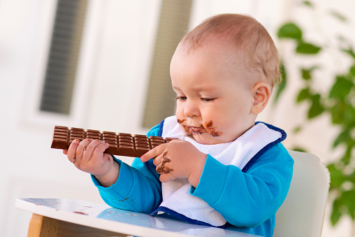 Baby boy eating chocolate.His face and hands smeared with chocolate.