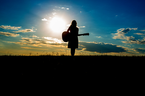 Silhouette woman playing guitar in the sunset