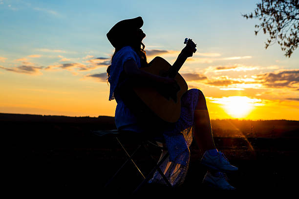 istock Beautiful young woman playing guitar at sunset 529144572