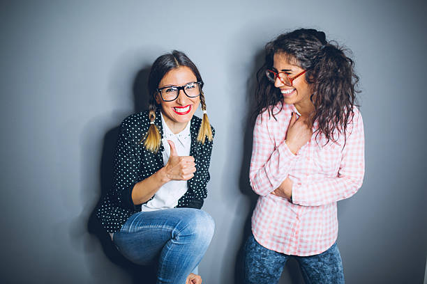 Two nerdy best friends giggling i studio on gray background