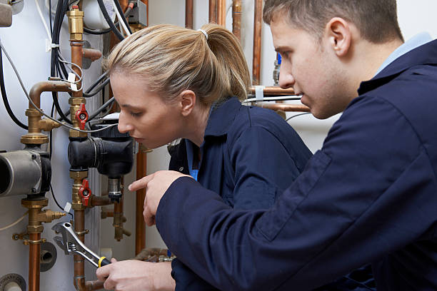 Female Trainee Plumber Working On Central Heating Boiler Female Trainee Plumber Working On Central Heating Boiler plumbing fixture stock pictures, royalty-free photos & images