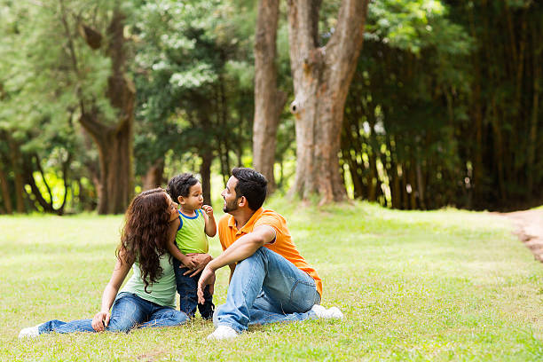 young family sitting outdoors young family of three sitting together outdoors happy indian young family couple stock pictures, royalty-free photos & images