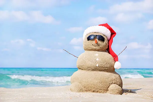Photo of Christmas snowman in santa hat at sandy beach
