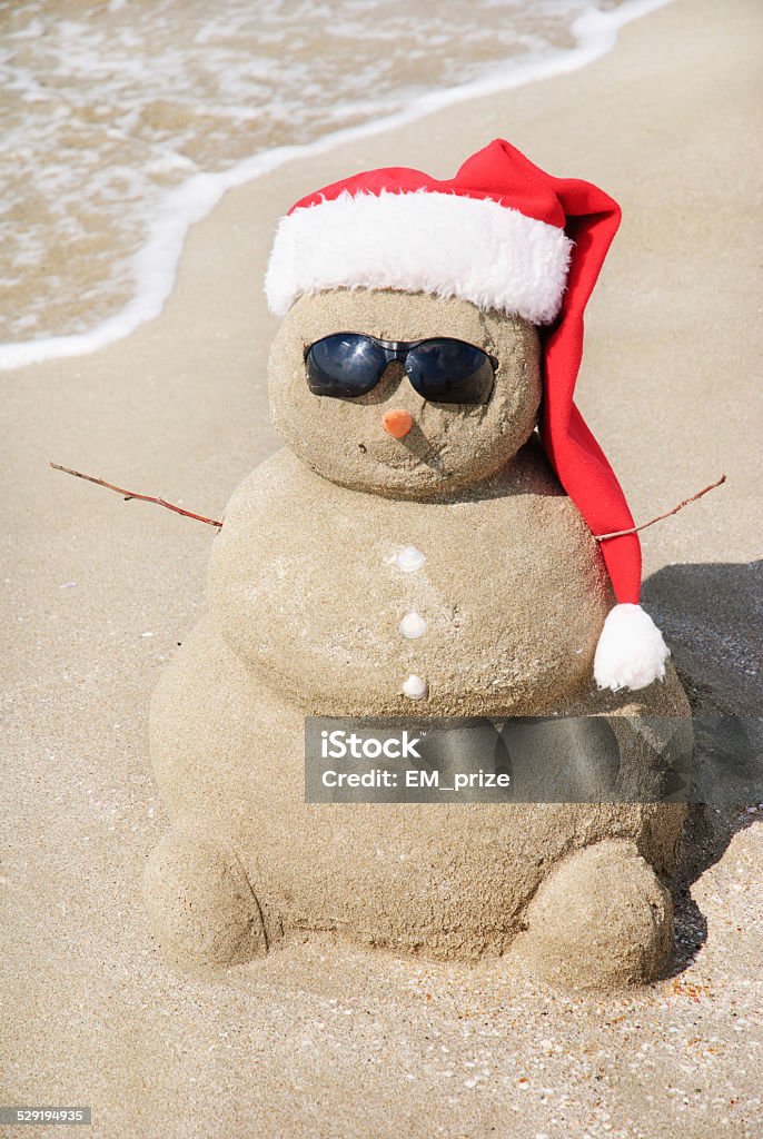 Navidad muñeco de nieve en santa sombrero en la playa de arena - Foto de stock de Agua libre de derechos