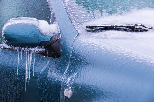 Frozen rearview mirror and wiper of the car with icicles, ice and frost