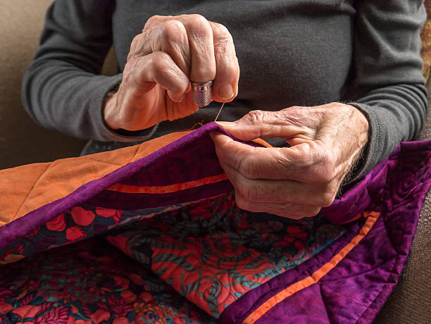 Senior Woman Expertly Stitches the Binding Onto Her Quilt stock photo