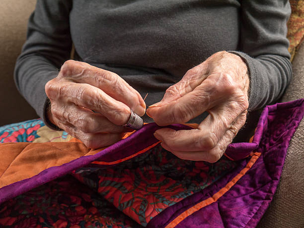 Senior Woman Expertly Stitches the Binding Onto Her Quilt stock photo