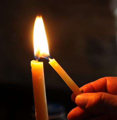 Human hand holding and lighting the candle in church for pray and make a wish.