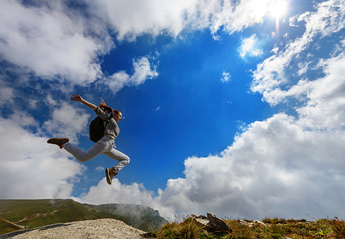 low angle view of woman jumping on mountain peak.