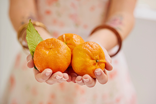 Cropped shot of three tangerines in a woman's hands
