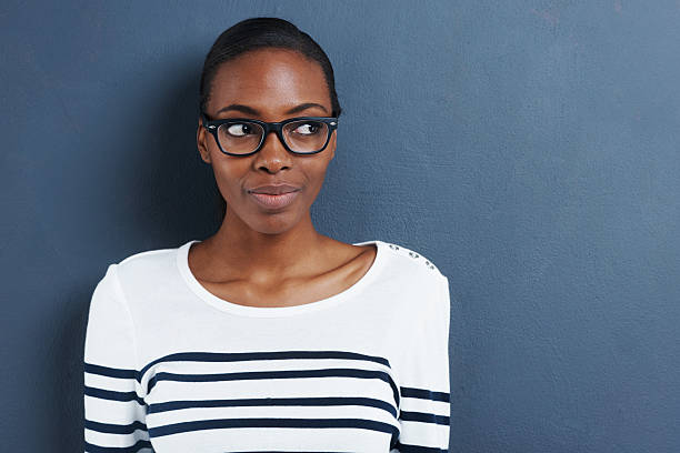 She's got her eye on you Shot of an attractive young woman wearing glasses glancing sideways on a gray background women satisfaction decisions cheerful stock pictures, royalty-free photos & images