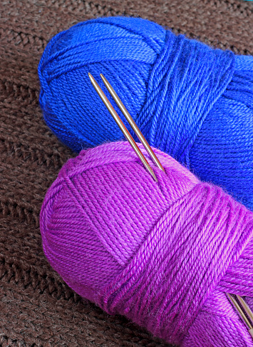 Two skeins of yarn with knitting needles on knitted background