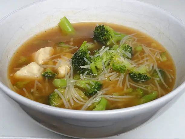 Photo showing a bowl of homemade chicken noodle soup / broth isolated on a white background. This is a low calorie meal made with broccoli and rice noodles, which are low in carbohydrate. This dish is part of a healthy eating, low fat diet plan.