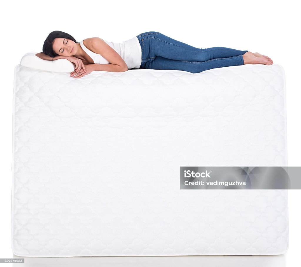 Sleeping Young woman is lying on the mattress. Isolated on white background. Side view.Smiling young woman with orthopedic mattress. Quality mattress.Smiling young woman with orthopedic mattress. Quality mattress. Mattress Stock Photo