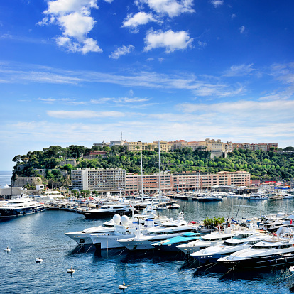 Monaco, Monte Carlo cityscape. Real estate architecture on mountain hill background. Many high-rise buildings in downtown area. Yachts moored at town quay In Sunny Summer Day.