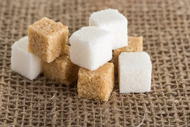 cubes white and brown cane sugar on a background of jute bags