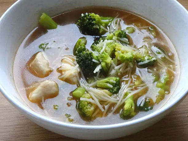Photo showing a bowl of homemade chicken noodle soup / broth on a table. This is a low calorie meal made with broccoli and rice noodles, which are low in carbohydrate. This dish is part of a healthy eating, low fat diet plan.