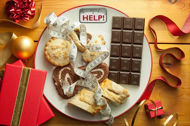 Plate with bathroom scales displaying the word help alongside Christmas foods and decorations