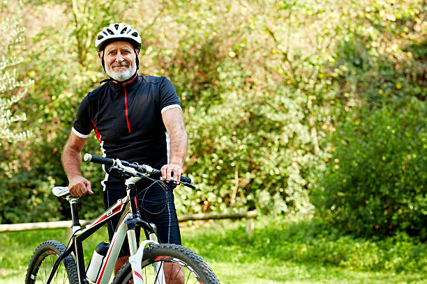 Confident senior man with bicycle in park Portrait of confident senior man standing with bicycle in park sports helmet photos stock pictures, royalty-free photos & images