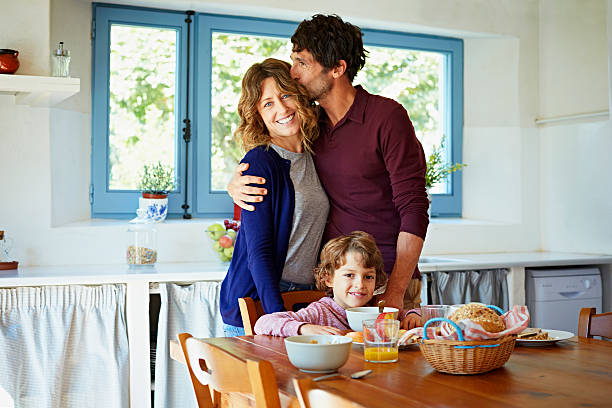 Loving family at breakfast table in kitchen Loving man kissing woman while standing behind son having breakfast at table in kitchen 40 49 years stock pictures, royalty-free photos & images