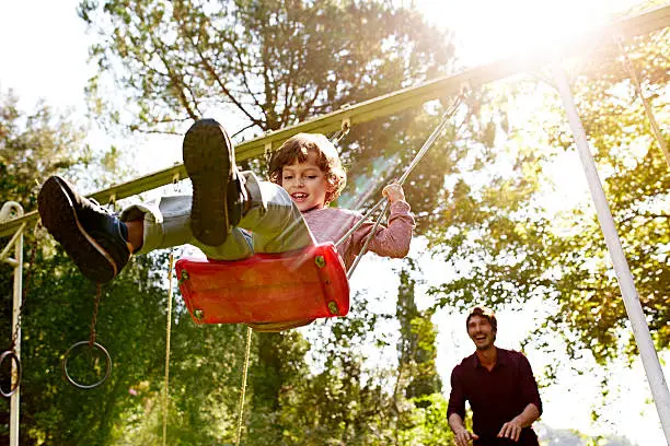 Photo of Father pushing son on swing in park