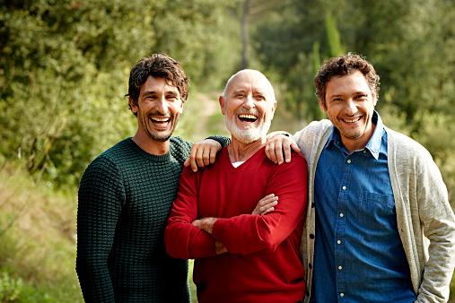 Portrait of cheerful senior man standing with sons at park