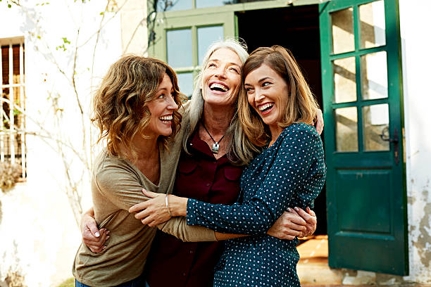 Mother and daughters embracing outdoors Playful mother and daughters embracing outside house women stock pictures, royalty-free photos & images