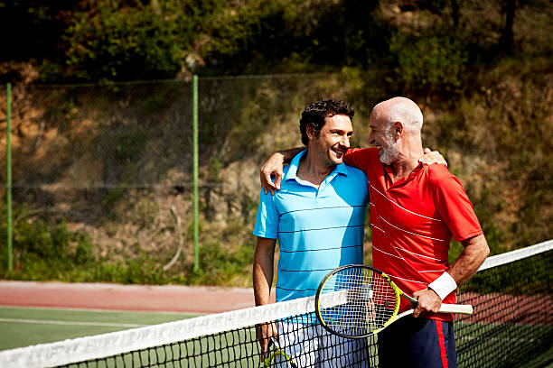 Happy father and son on tennis court Happy father and son looking at each other on tennis court tennis senior adult adult mature adult stock pictures, royalty-free photos & images