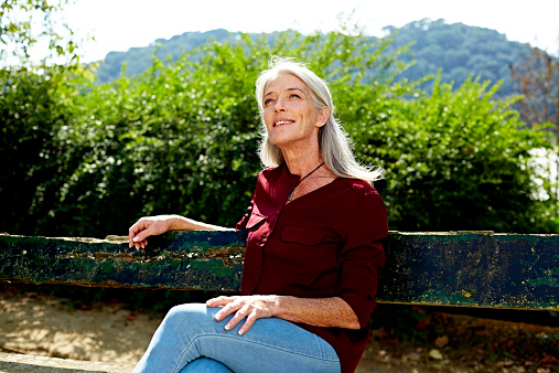 Thoughtful senior woman looking away while sitting on bench in park