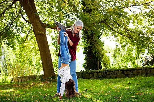 Grandmother assisting granddaughter in doing handstand at park