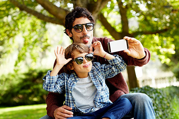 playful father and son taking selfie in park - far fotografier bildbanksfoton och bilder