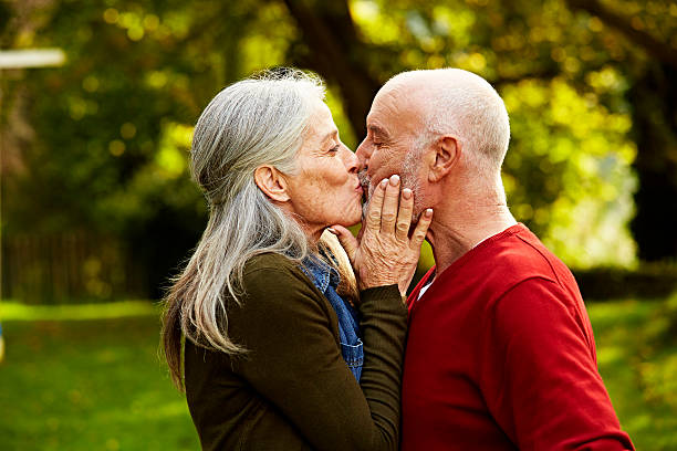 senior couple kissing at park - küssen stock-fotos und bilder
