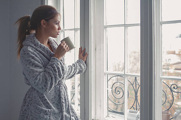 istock Young woman drinks morning coffee, looking through the window 529371043