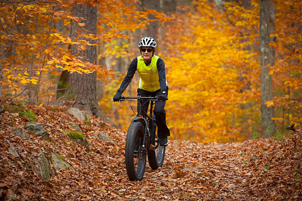 Attractive woman riding a fatbike on leaf covered trail stock photo