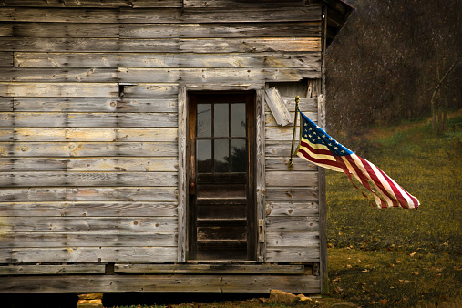 American Flag hanging from an old barn with negative space to display text.