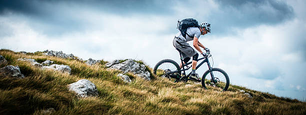 Biker Riding on a Mountain Trail Low angle view of a mountain biker riding bike on a mountain trail along the edge of a ridge. mountain biking stock pictures, royalty-free photos & images