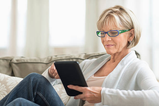 donna utilizzando computer tablet sul divano - solo una donna matura foto e immagini stock