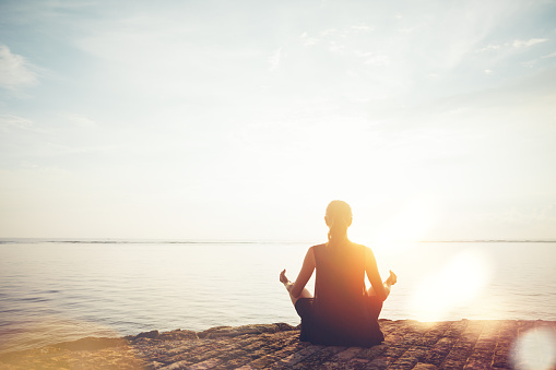 Young woman doing meditation practice on the beach. Intentional sun glare and lens flare effect
