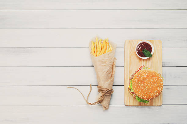 Burger, chips and ketchup at white wood Burger and Chips. Hamburger and french fries wrapped in brown wrapping paper. Fast food take away at white shabby chic wood. Hamburger with tomato sauce. Top view, flat lay with copyspace white shabby chic desk stock pictures, royalty-free photos & images